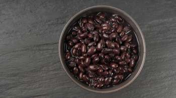 A bowl of black beans in liquid on a dark stone surface.
