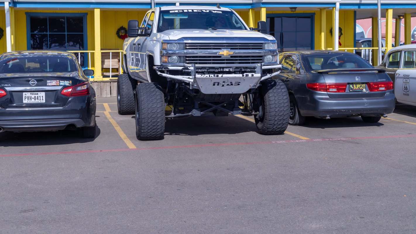 A large lifted pickup truck parked between two smaller cars in a parking lot.