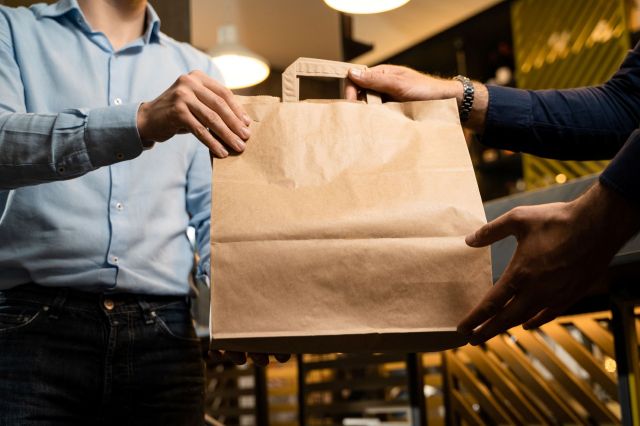 A person hands another person a brown paper bag in a restaurant.
