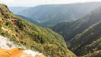 A green valley with steep mountains and a waterfall.