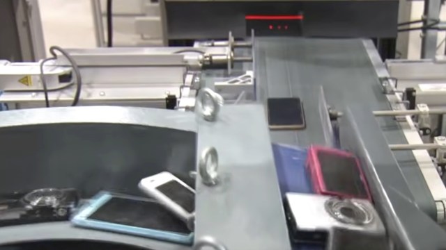 A conveyor belt transports various electronic devices, including smartphones and cameras, in a processing facility.