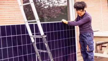 A technician installs a solar panel while a ladder stands nearby on a residential patio.
