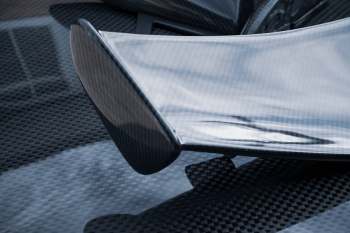 A close-up of a sleek carbon fiber car spoiler on a textured surface.