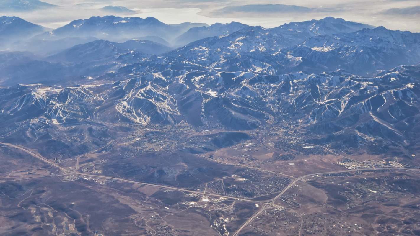 Aerial view of rugged snow-capped mountains with valleys and roads below.