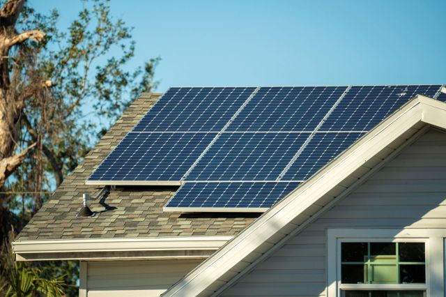 A house roof featuring solar panels with clear blue sky and trees in the background.