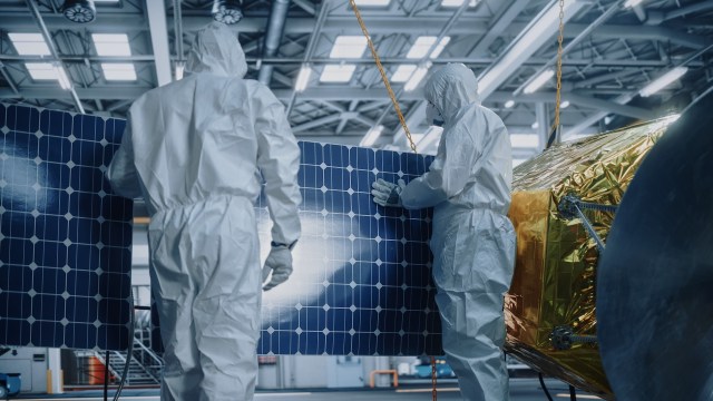 Two workers in white protective suits handle a large solar panel.