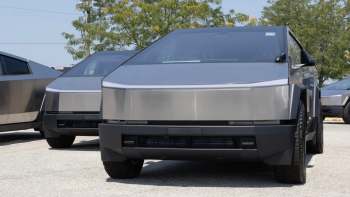 Two futuristic, angular Tesla Cybertrucks with stainless steel exteriors parked in a lot under a clear sky.