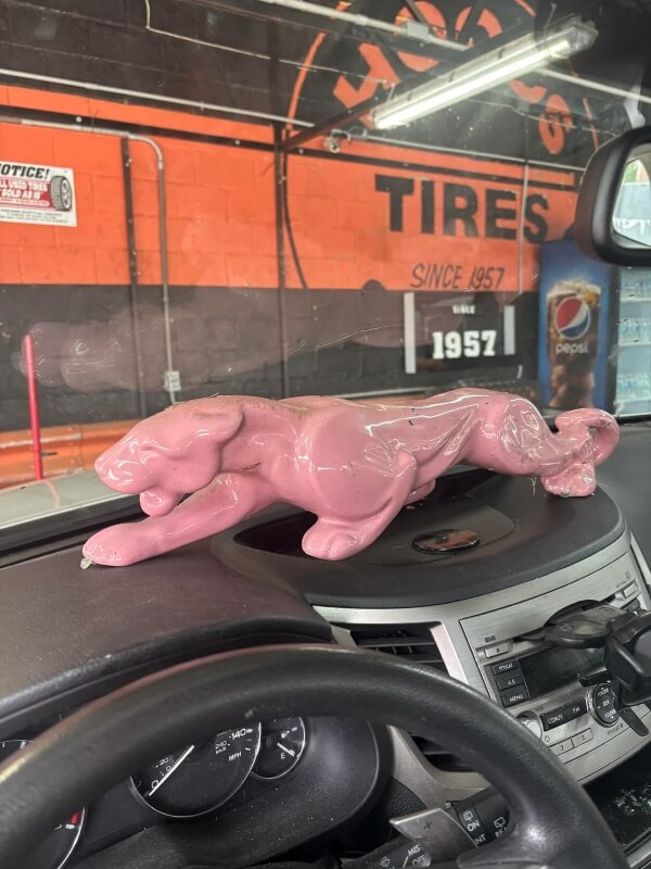 A pink panther statue sitting on a car's dashboard in front of a red and  black-striped wall.