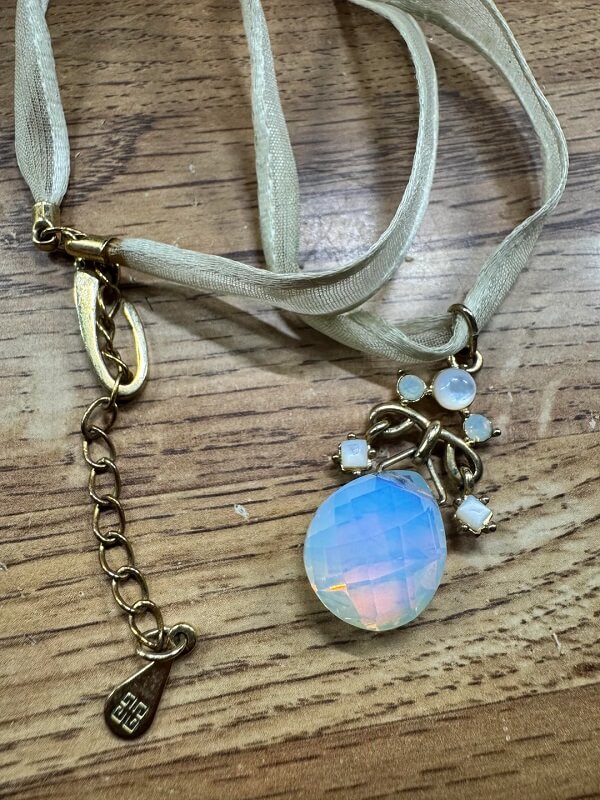 A delicate ribbon necklace with a gold pendant featuring blue and white gemstones.