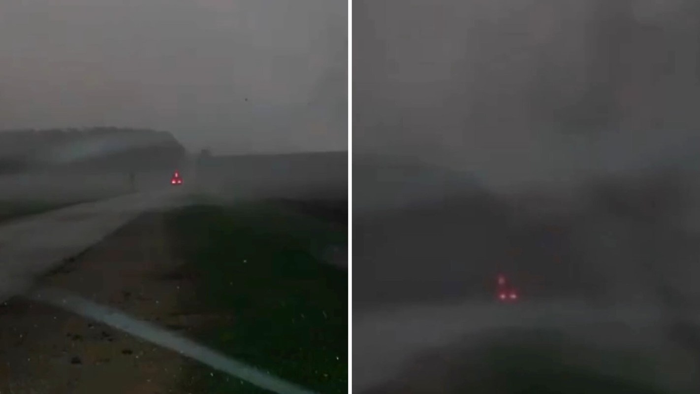 A dimly lit road shrouded in a tornado with the red lights of a vehicle faintly visible in the distance.