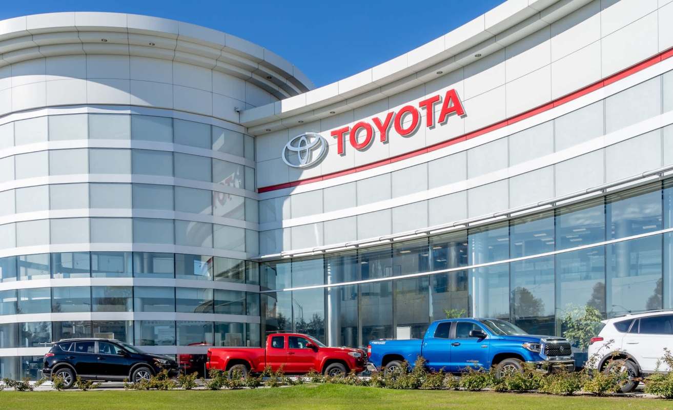 A modern Toyota dealership with a variety of vehicles displayed in front, including red, blue, and black trucks.