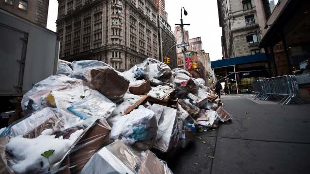 A large pile of trash bags and cardboard boxes stacked on a city street.