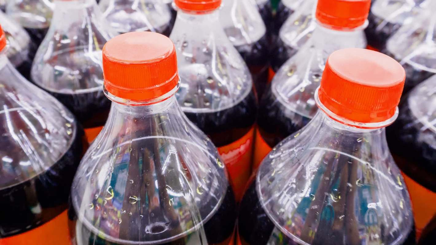 A close-up of multiple plastic soda bottles with red caps, showing condensation on the surface.