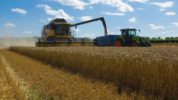 A thresher harvesting wheat on a farm with blue sky and clouds above.