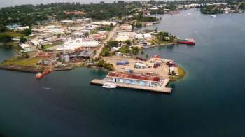 Aerial view of a coastal area with warehouses, boats, and surrounding greenery.