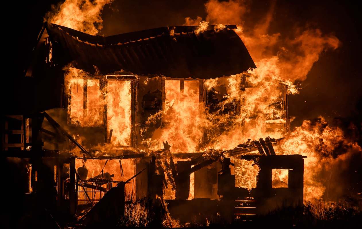 A house engulfed in flames, with bright orange fire and smoke filling the scene against a dark background.