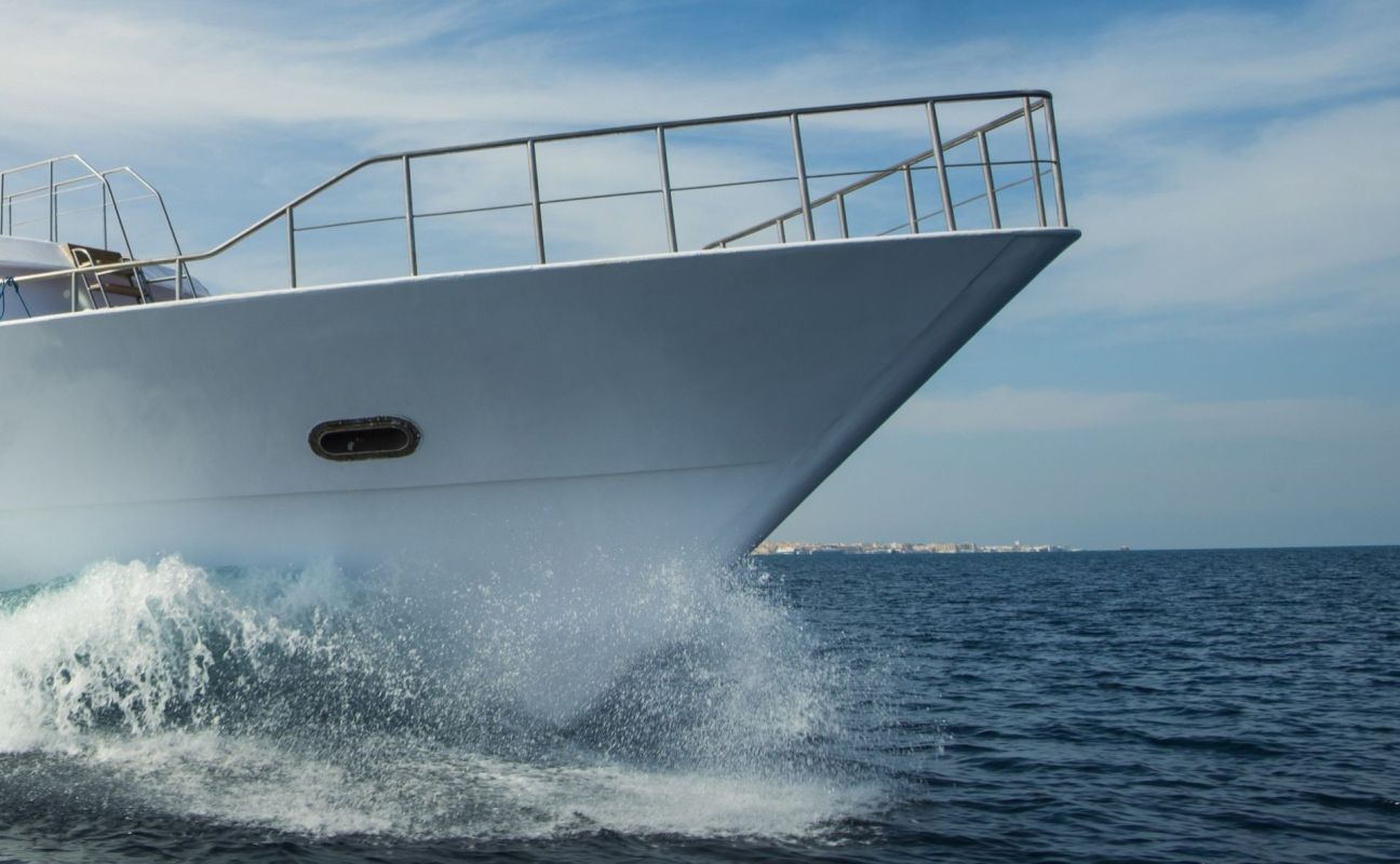The bow of a boat cutting through ocean waves with a clear blue sky in the background.
