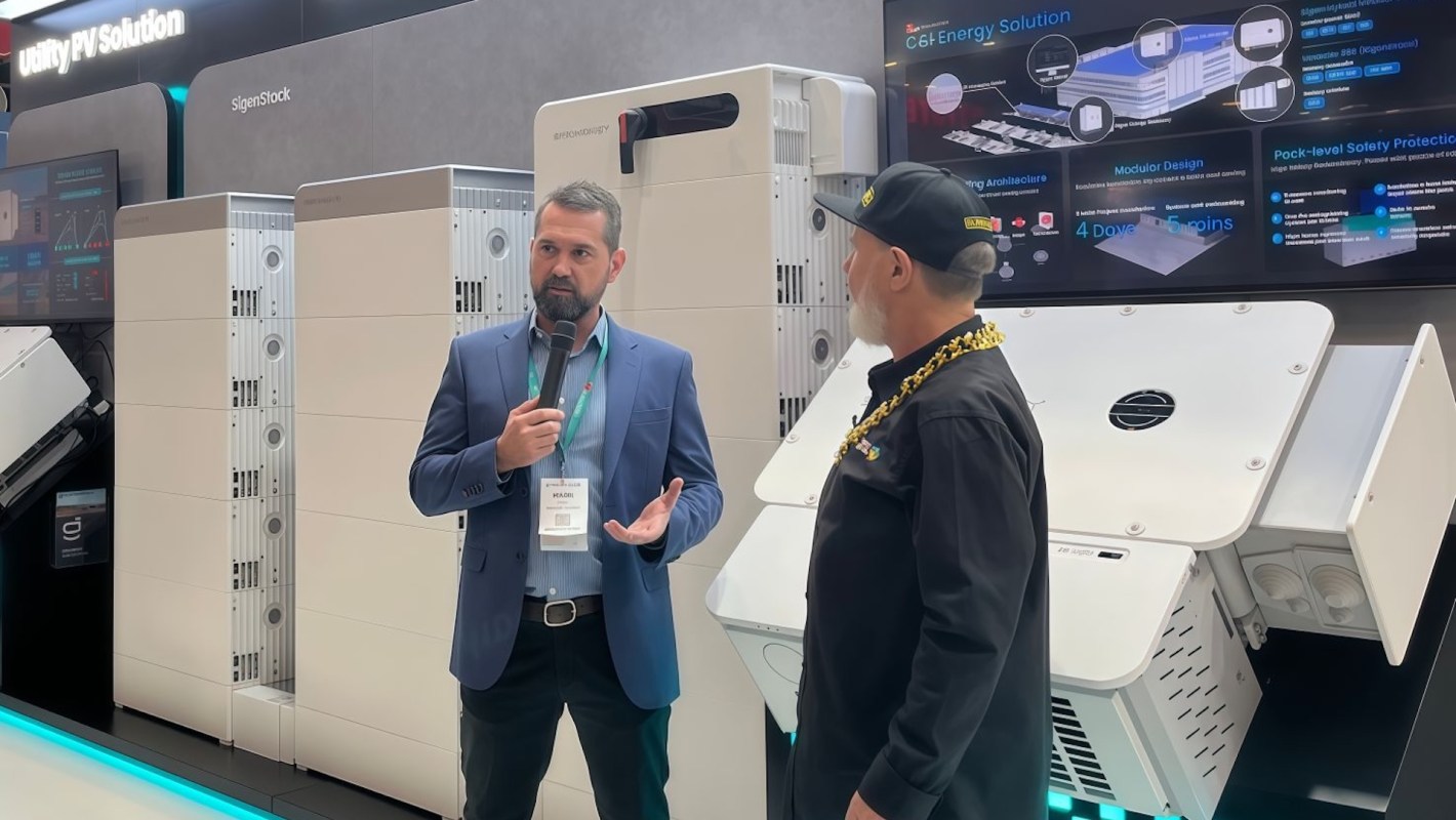 Two men are discussing solar energy solutions in front of large energy storage units at a trade show.