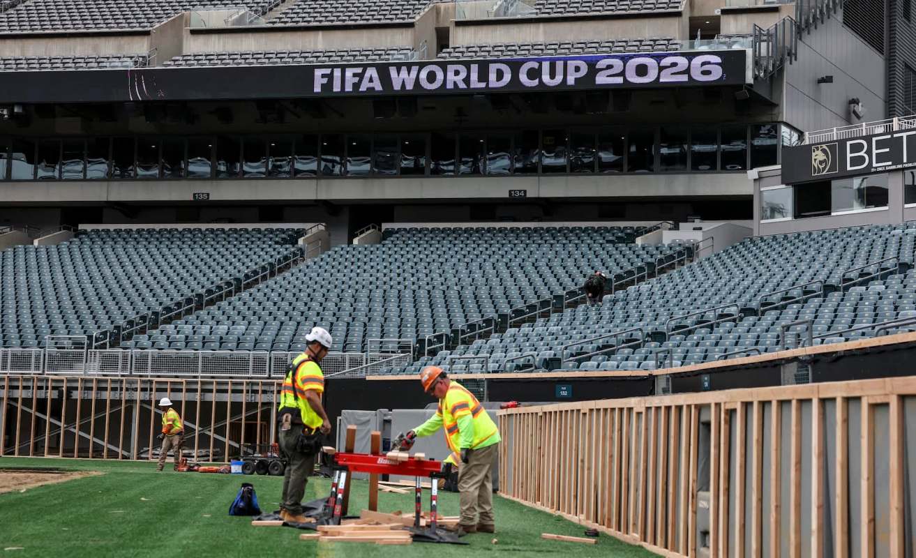 Construction workers prepare a stadium for the FIFA World Cup 2026, with empty seats in the background.