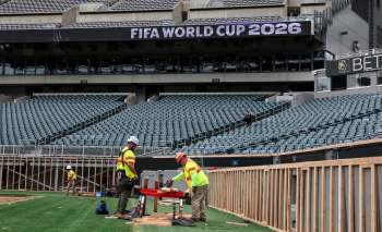 Construction workers prepare a stadium for the FIFA World Cup 2026, with empty seats in the background.