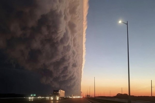 A dramatic shelf cloud looms over a highway at sunset.
