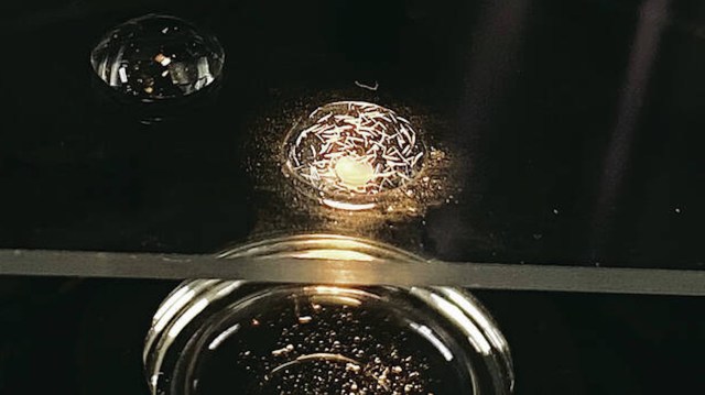 Two droplets on a dark surface, reflecting light.
