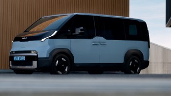 A modern, two-tone Kia electric van parked near a building with a textured brown wall.