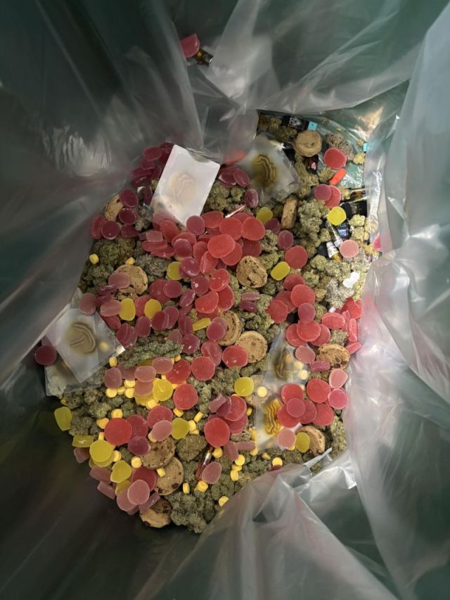 A large, colorful collection of cannabis flower, gummies, cookies, vape cartridges, and more in a plastic trash bag. 