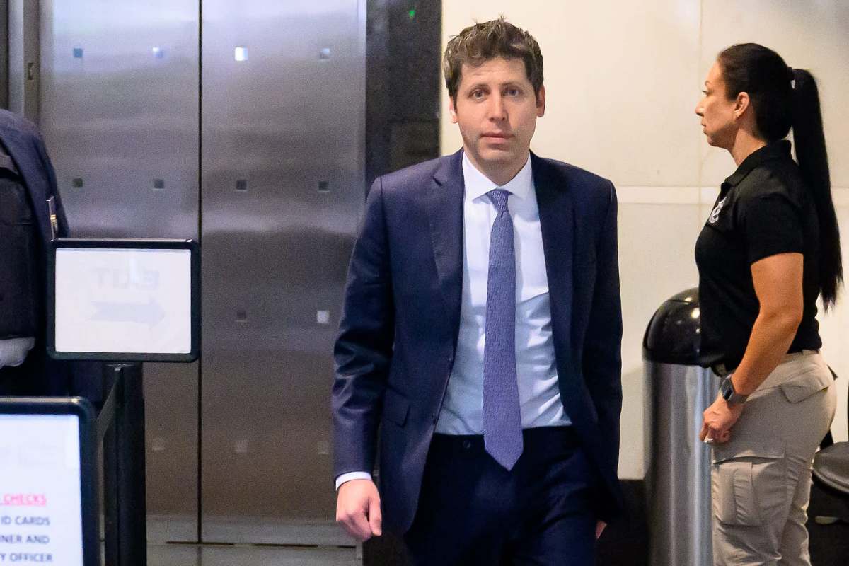 Sam Altman walks toward an exit with a security officer standing nearby.
