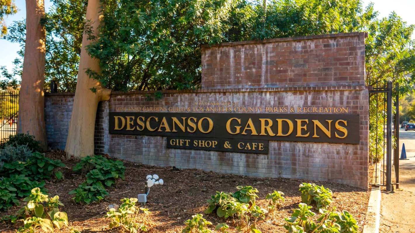 A brick entrance sign for Descanso Gardens, featuring a gift shop and café, surrounded by greenery.