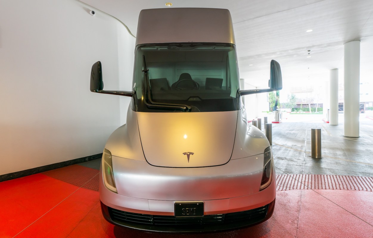 A front view of a silver Tesla Semi truck parked indoors, with a red floor and white walls in the background.