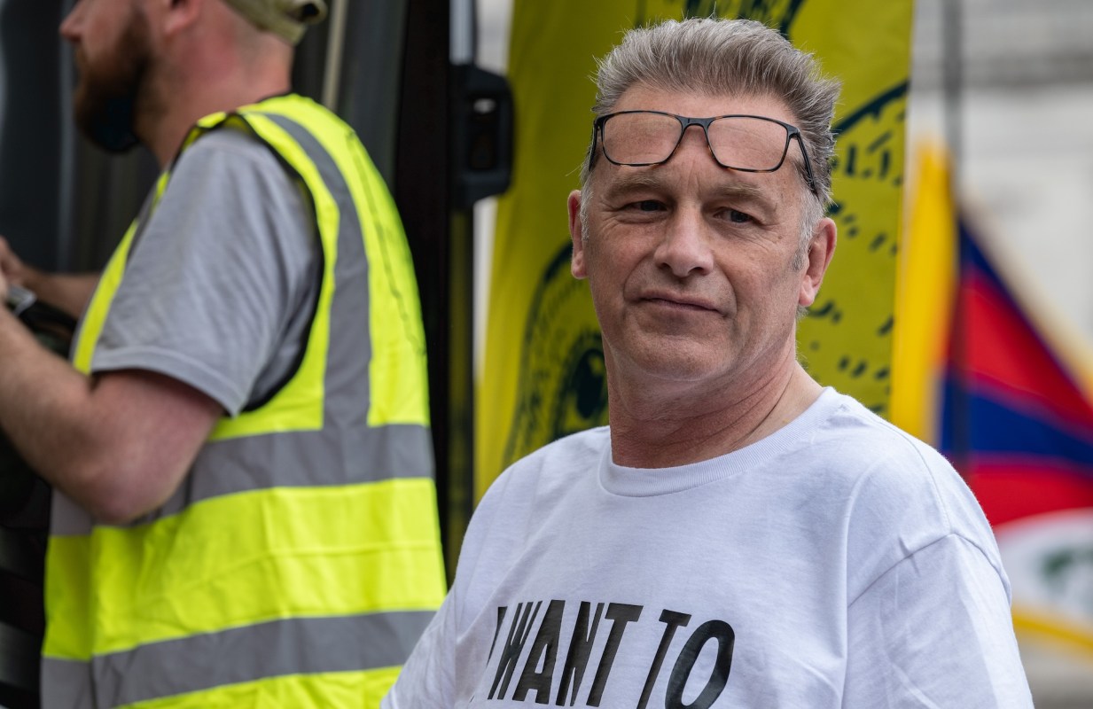 Chris Packham, wearing a white shirt and glasses on his forehead, stands near a yellow flag.