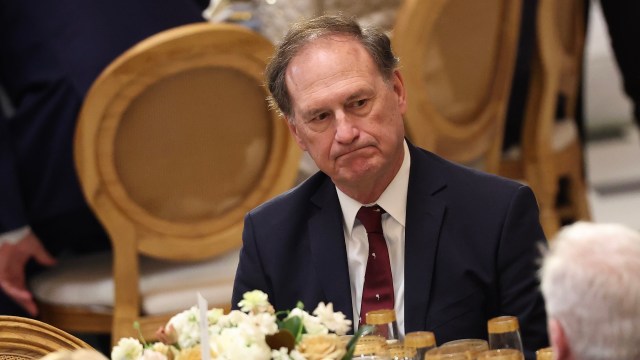 U.S. Supreme Court Justice Samuel Alito, in a suit, sits at a table with a pensive expression.
