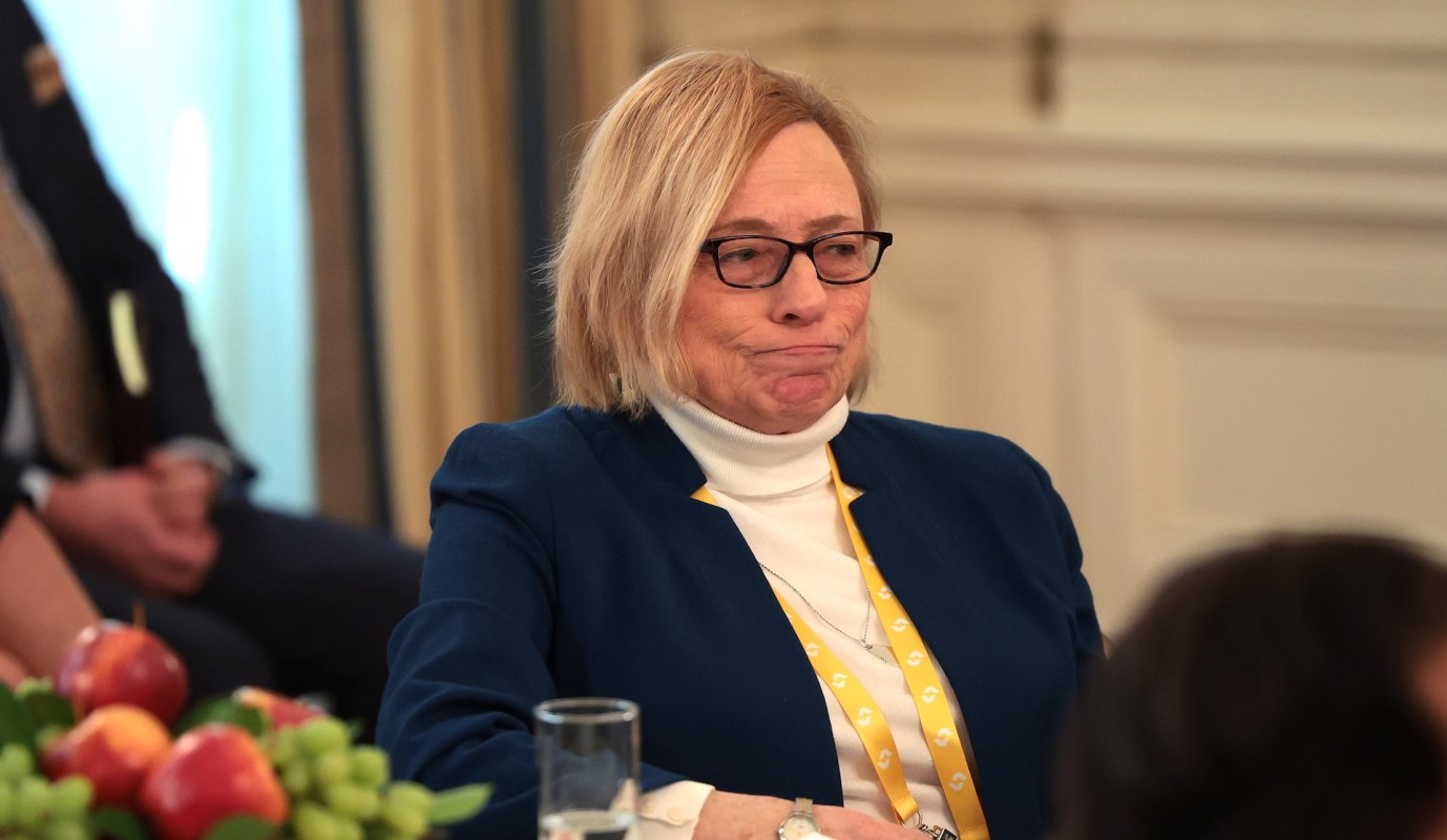 Maine Governor Janet Mills, wearing glasses, looks contemplative while seated at a table with fruit, wearing a blue jacket.