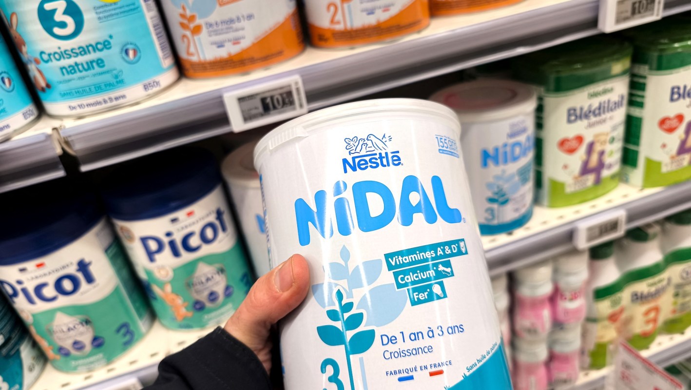 A person holds a jar of Nestlé Nidal powdered infant formula labeled for children aged 1 to 3 years.
