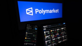 A smartphone displaying the Polymarket platform, with a logo in the background on a computer screen.