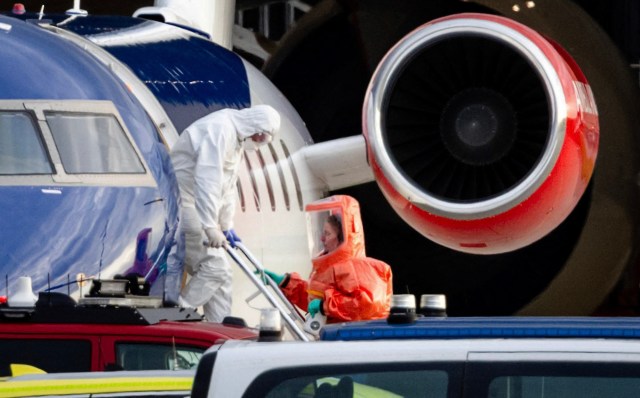 Two workers in protective suits attend to an aircraft at an airport.
