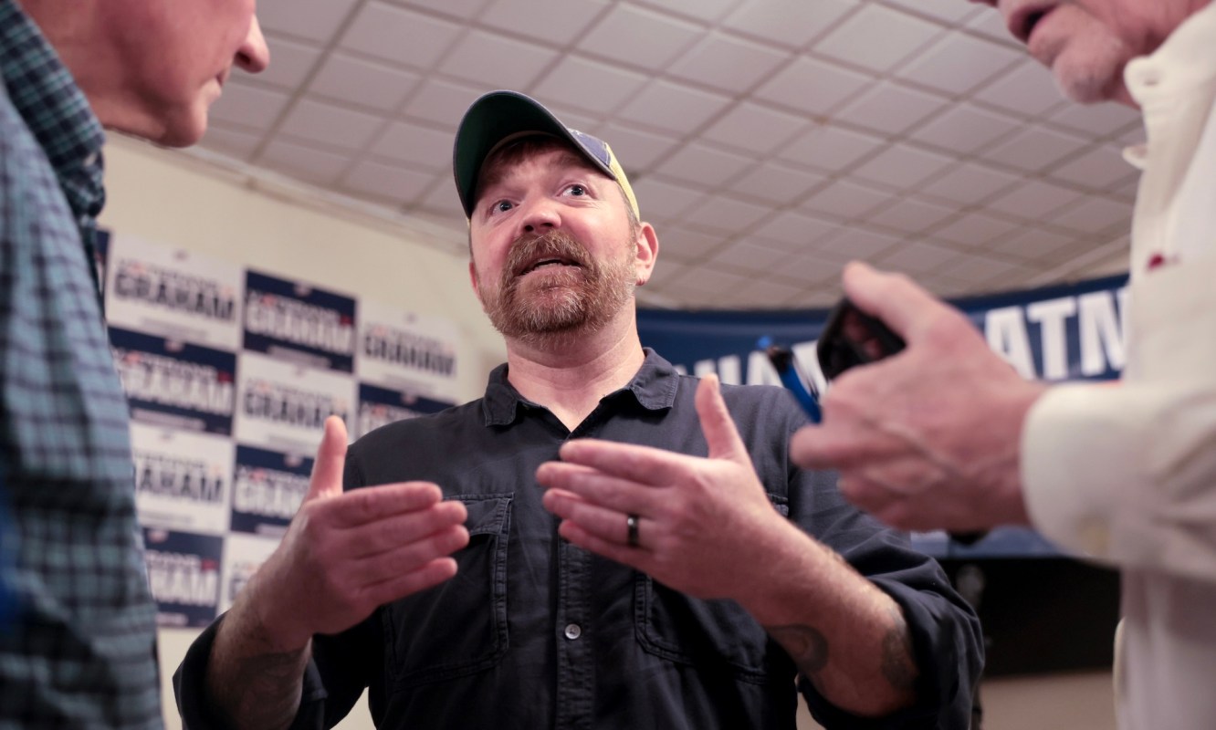U.S. Senate candidate Graham Platner, with a beard, gestures while talking with two others in a room.