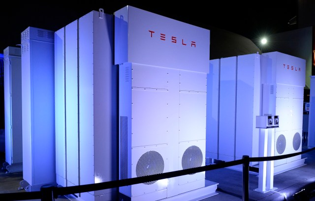 Three Tesla energy storage units illuminated with blue lighting, displaying a sleek white design.