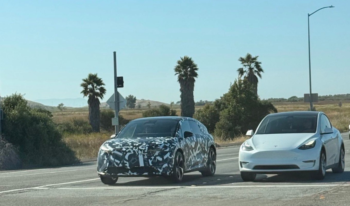 A camouflaged Lucid Cosmos prototype and a white Tesla Model Y at an intersection.