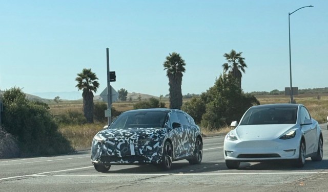 A camouflaged Lucid Cosmos prototype and a white Tesla Model Y at an intersection.