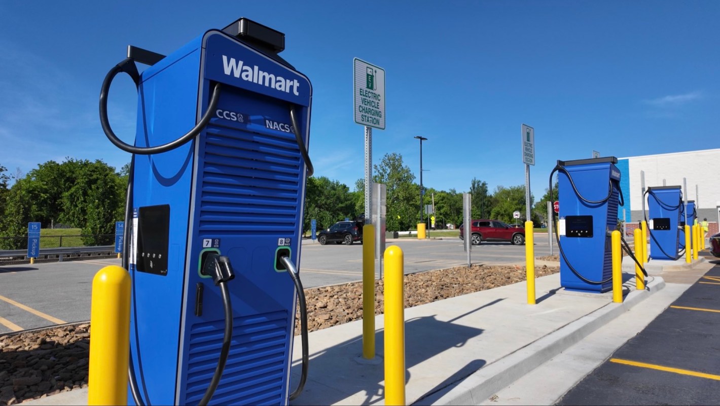 Three blue electric vehicle charging stations in a Walmart parking lot under a clear blue sky.