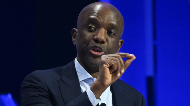Google SVP James Manyika gestures while speaking in front of a black and blue background.