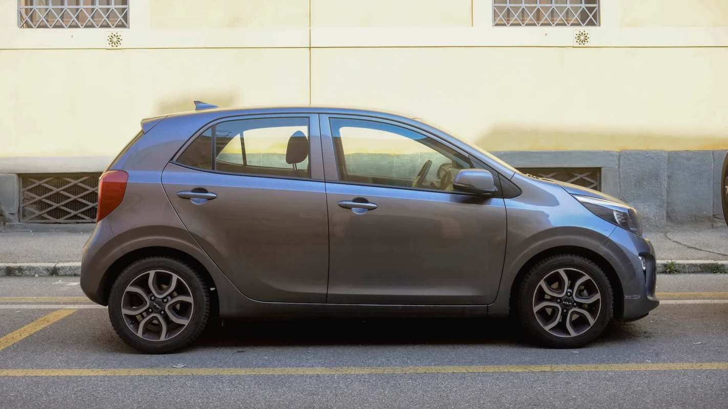A gray compact car parked on a city street beside a muted yellow building.