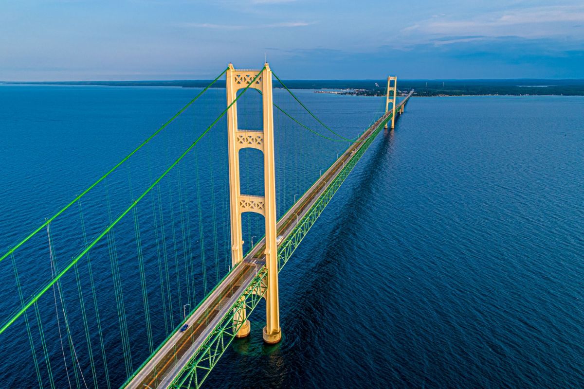Aerial view of a large suspension bridge crossing over a deep blue body of water under a clear sky.