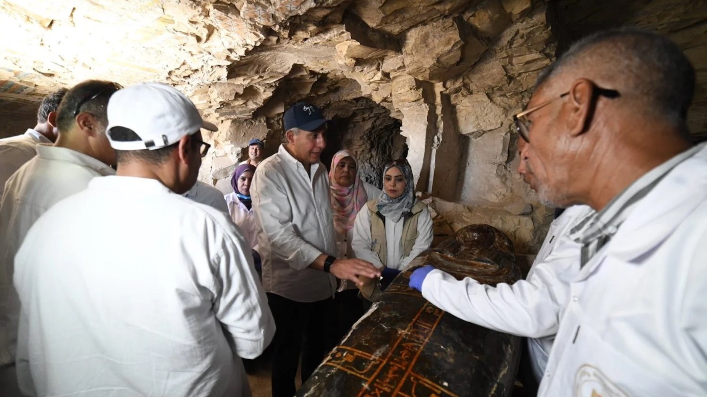 A group of researchers examines an ancient sarcophagus inside a stone cave.