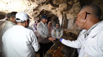 A group of researchers examines an ancient sarcophagus inside a stone cave.