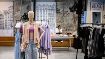 A mannequin displays casual apparel in a Shein retail store, with hanging clothes and a seated employee in the background.