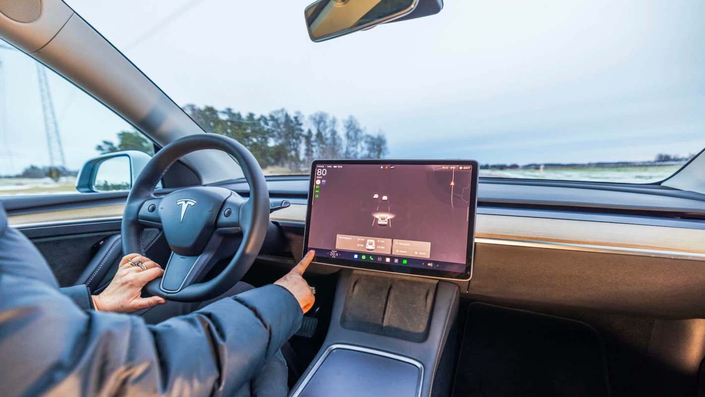 A person interacts with a touchscreen display in a Tesla car's modern interior while driving.