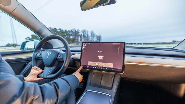 A person interacts with a touchscreen display in a Tesla car's modern interior while driving.